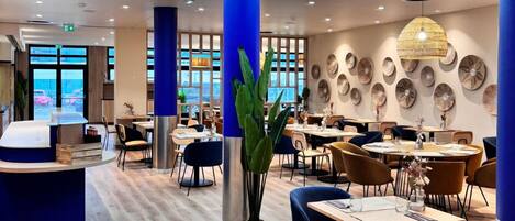 Un restaurante moderno con una recepción central, suelo de madera, sillas azules y marrones, y un amplio tragaluz.