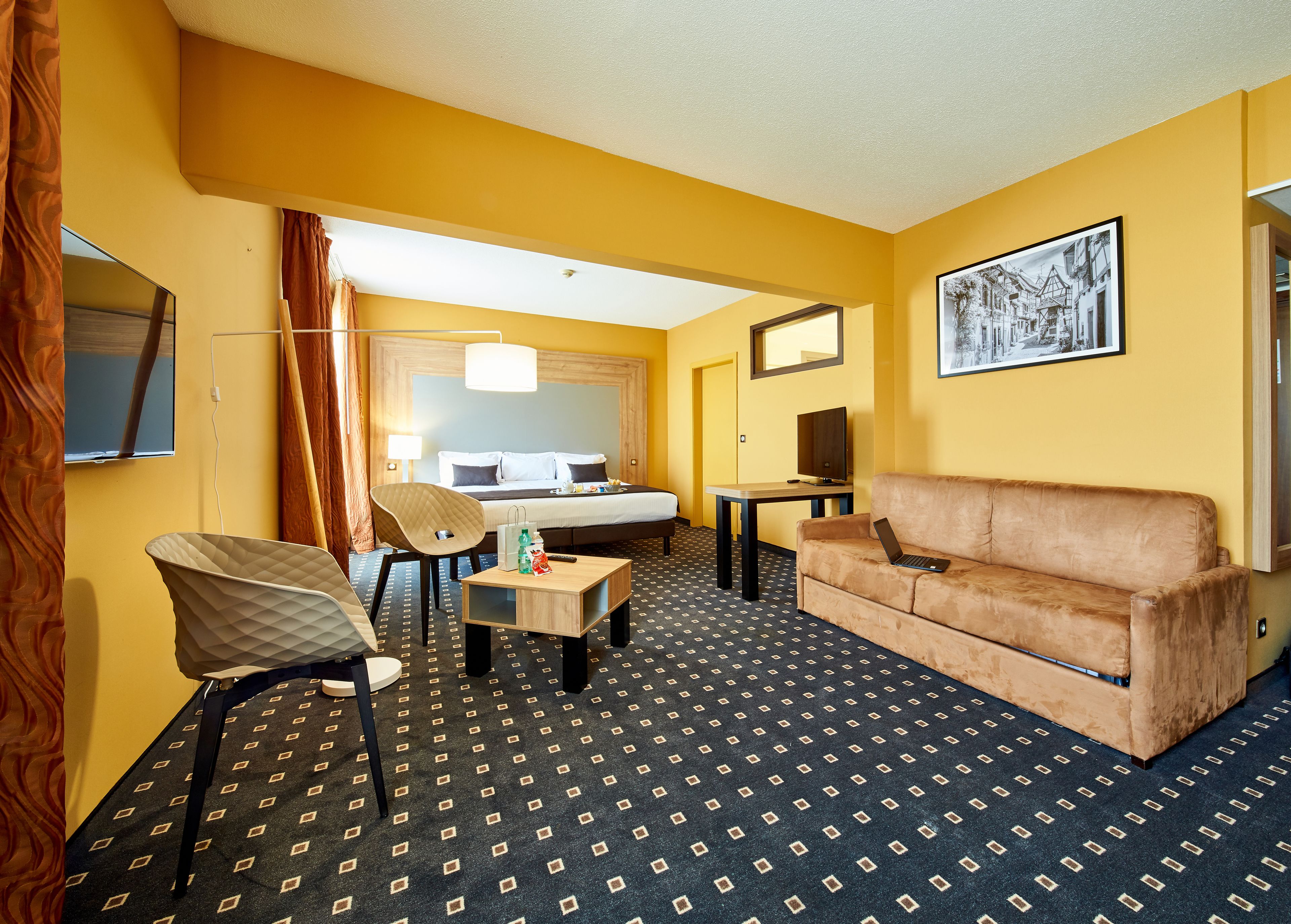 A hotel room with a bed, a sofa, a desk, a chair, and a TV.