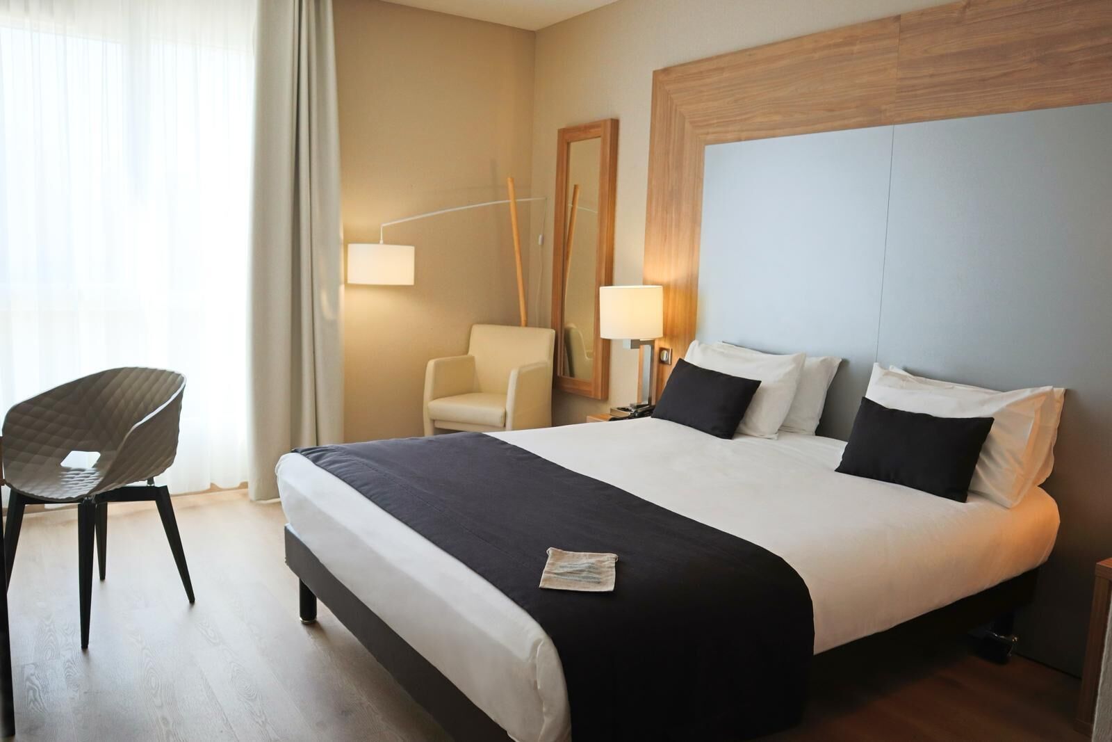 A hotel room with a large bed, a chair, a desk, and a lamp.