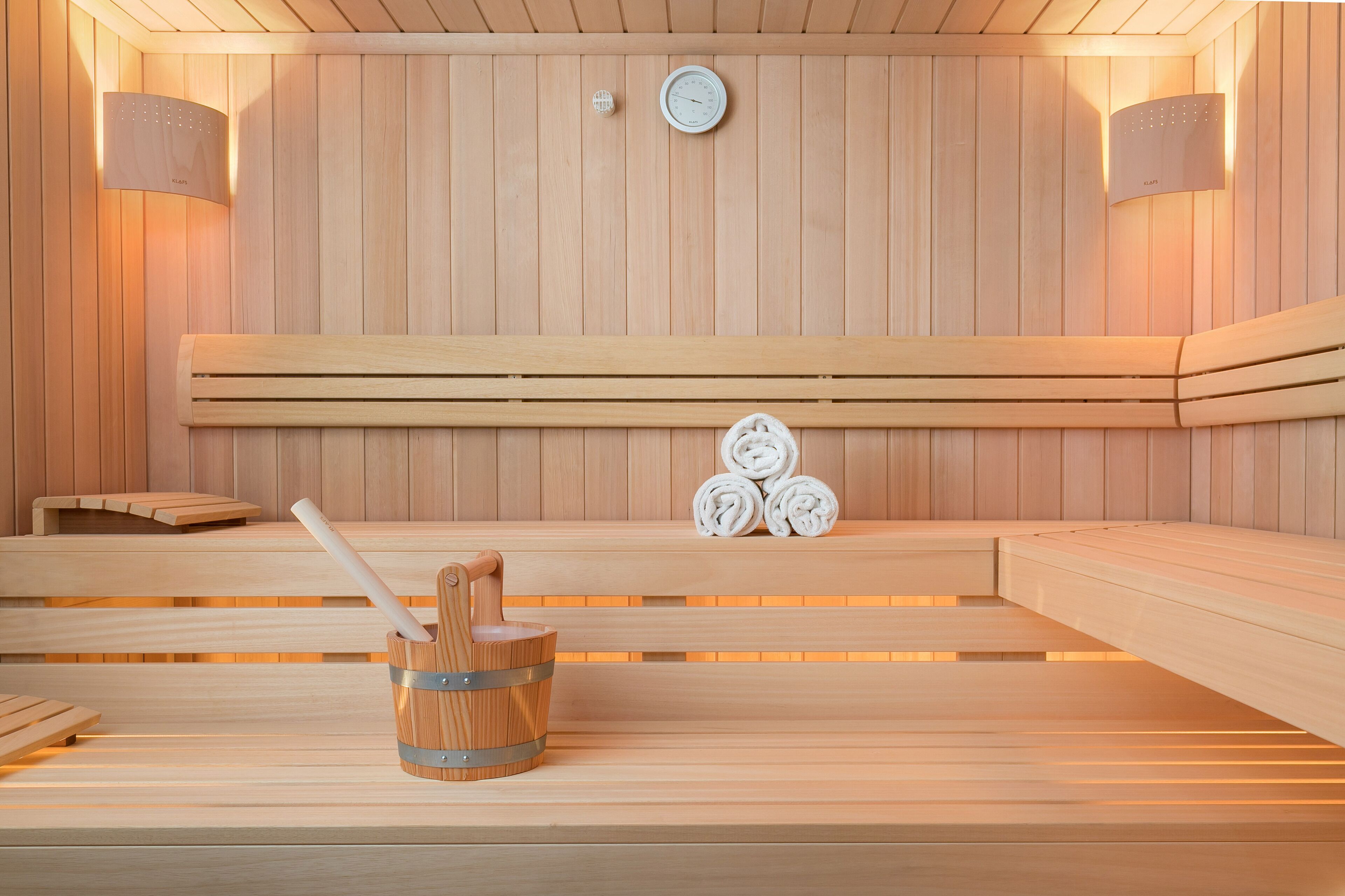Eine Holzsauna mit Bänken, einer Uhr und einem Eimer mit einem Besen.