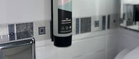 A bathroom with a white tiled wall, a bottle of Esteban Paris Parfums gel, and a mirror.