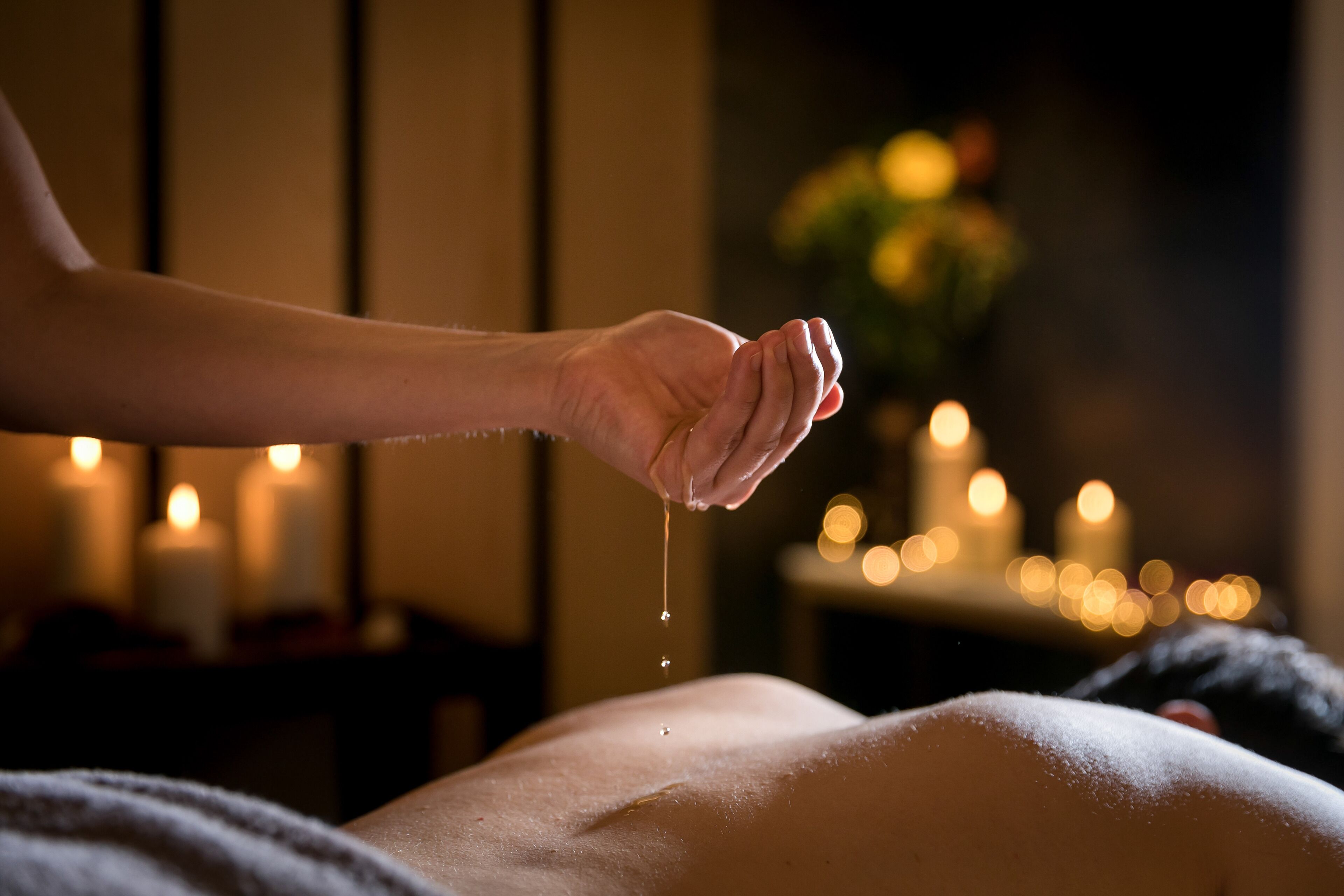 A hand holding a drop of liquid over a person's back in a dimly lit room with candles.