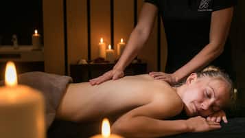 Eine Person erhält eine Massage in einem schwach beleuchteten Raum mit Kerzen.