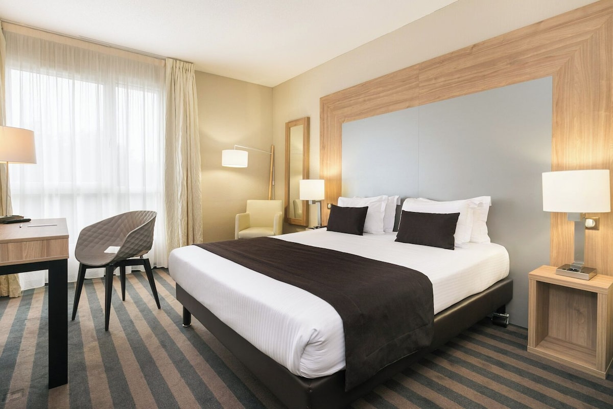 Une chambre d’hôtel avec un grand lit, un bureau, une chaise et une table de chevet avec une lampe.