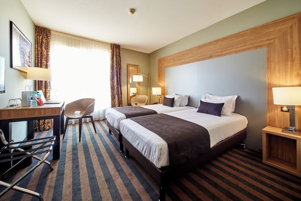 Une chambre d’hôtel avec deux lits, un bureau avec une chaise, une petite table et une lampe.