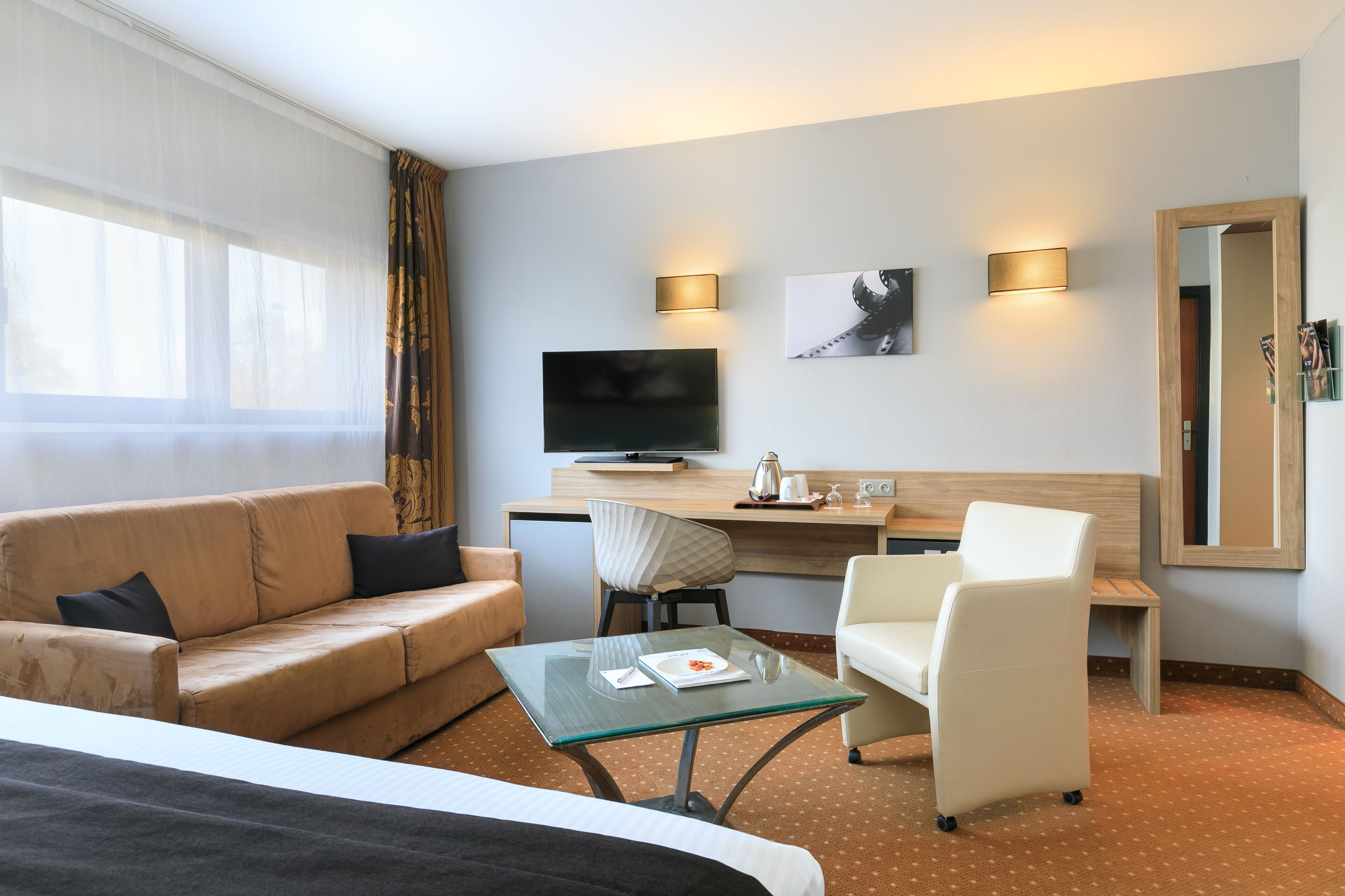 Una habitación de hotel con una cama, un sofá, un escritorio con televisor, una silla y una mesita.