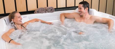 A couple relaxing in a hot tub with wooden paneling in the background.
