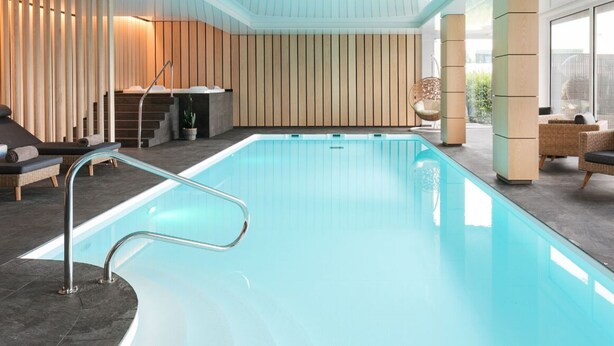 A modern indoor pool area with a clear pool, lounge chairs, and a wooden wall design. - 7Hotel&Spa (Illkirch-Graffenstaden)