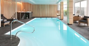 Un área de piscina interior moderna con una piscina cristalina, sillas de descanso y un diseño de pared de madera.