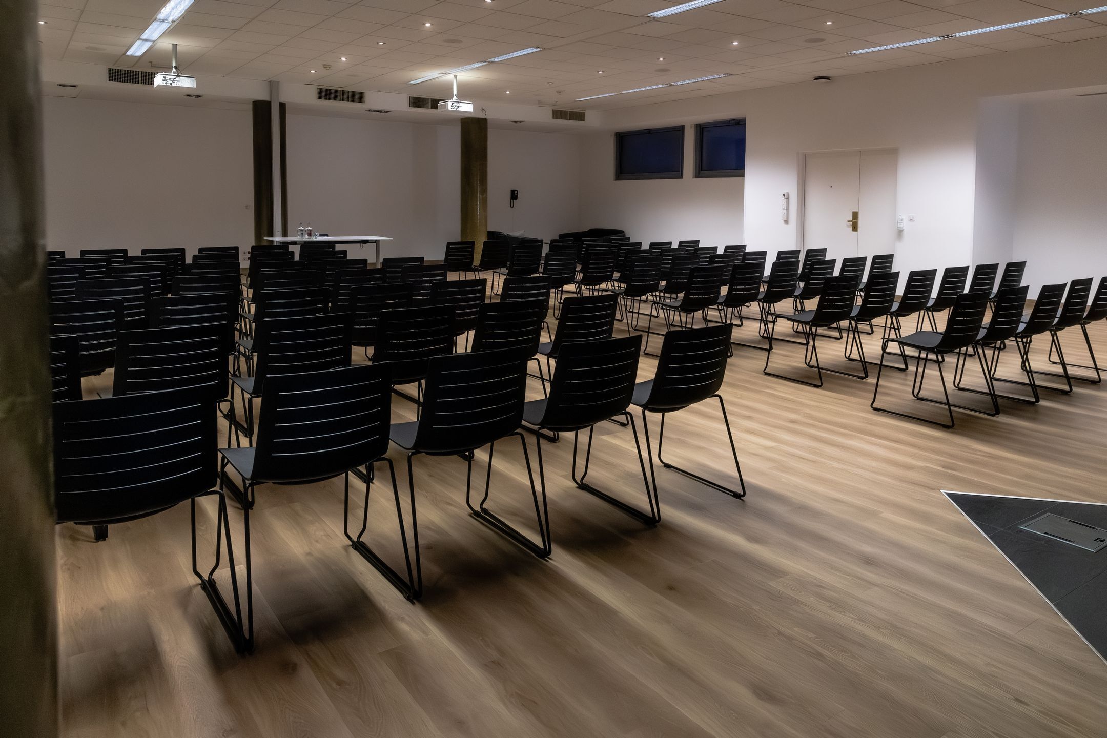 Konferenssihuone, jossa on riveissä mustia tuoleja, valkoinen pöytä ja projektorikangas.