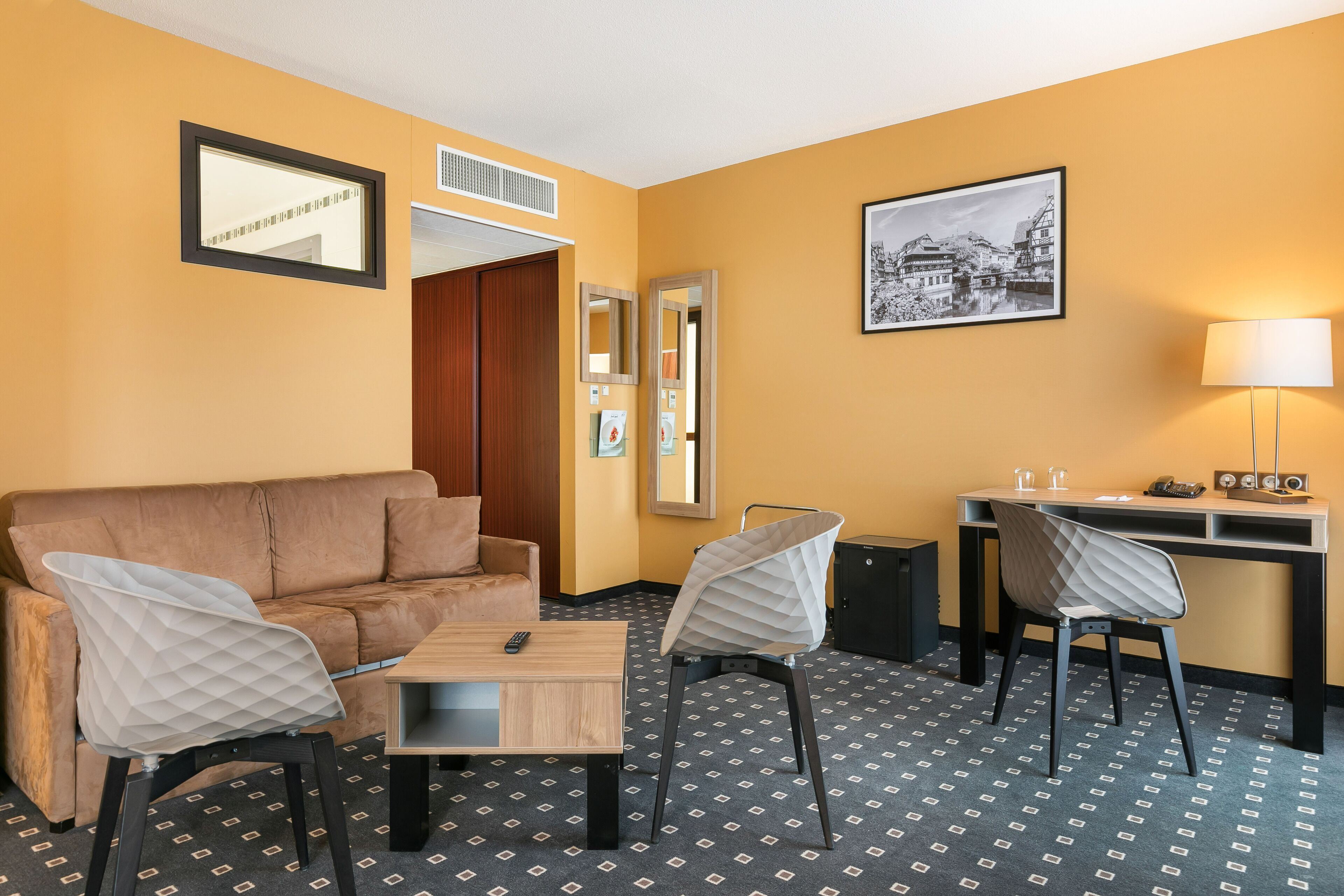 Une chambre d’hôtel avec un canapé, deux fauteuils, un bureau, une lampe et un tapis à motifs.