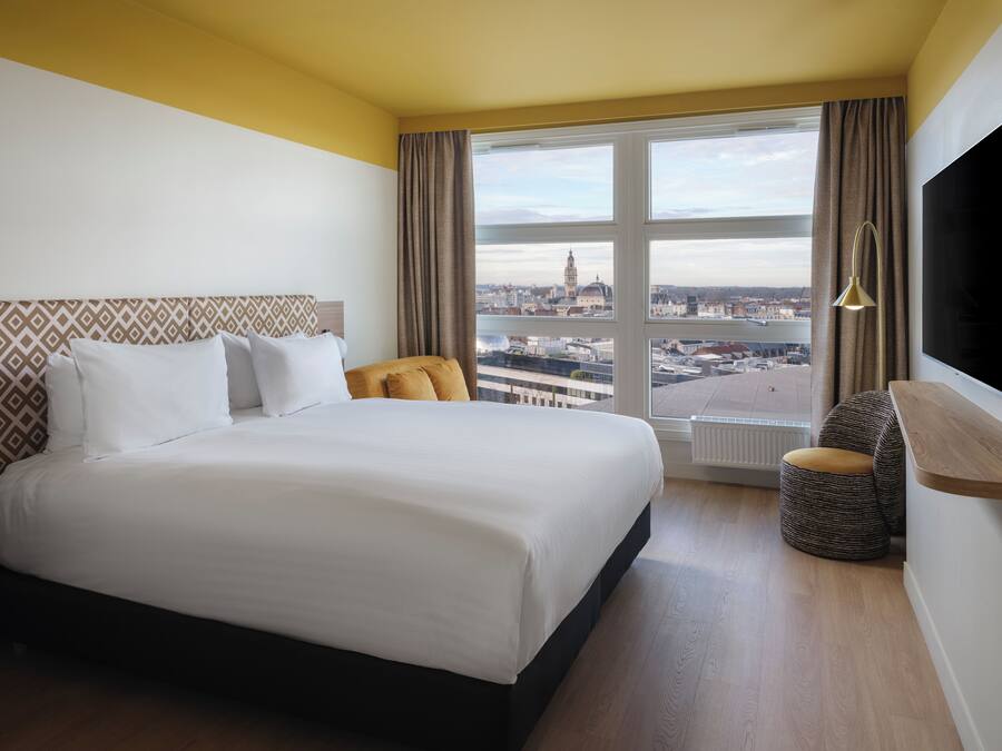 Une chambre d’hôtel avec un grand lit, une vue sur la ville, une télévision et un petit coin salon.