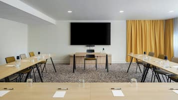 A conference room with a large table, chairs, a TV screen, and a carpeted floor.