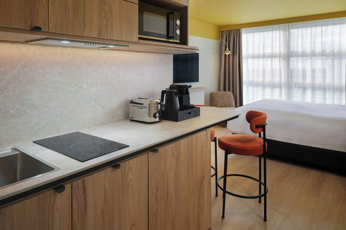 Habitación de hotel con kitchenette, cama, televisor y ventana con cortinas.