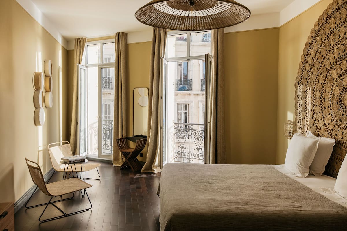 A hotel room with a large bed, a chair, a small table, and a view of the outside balcony.