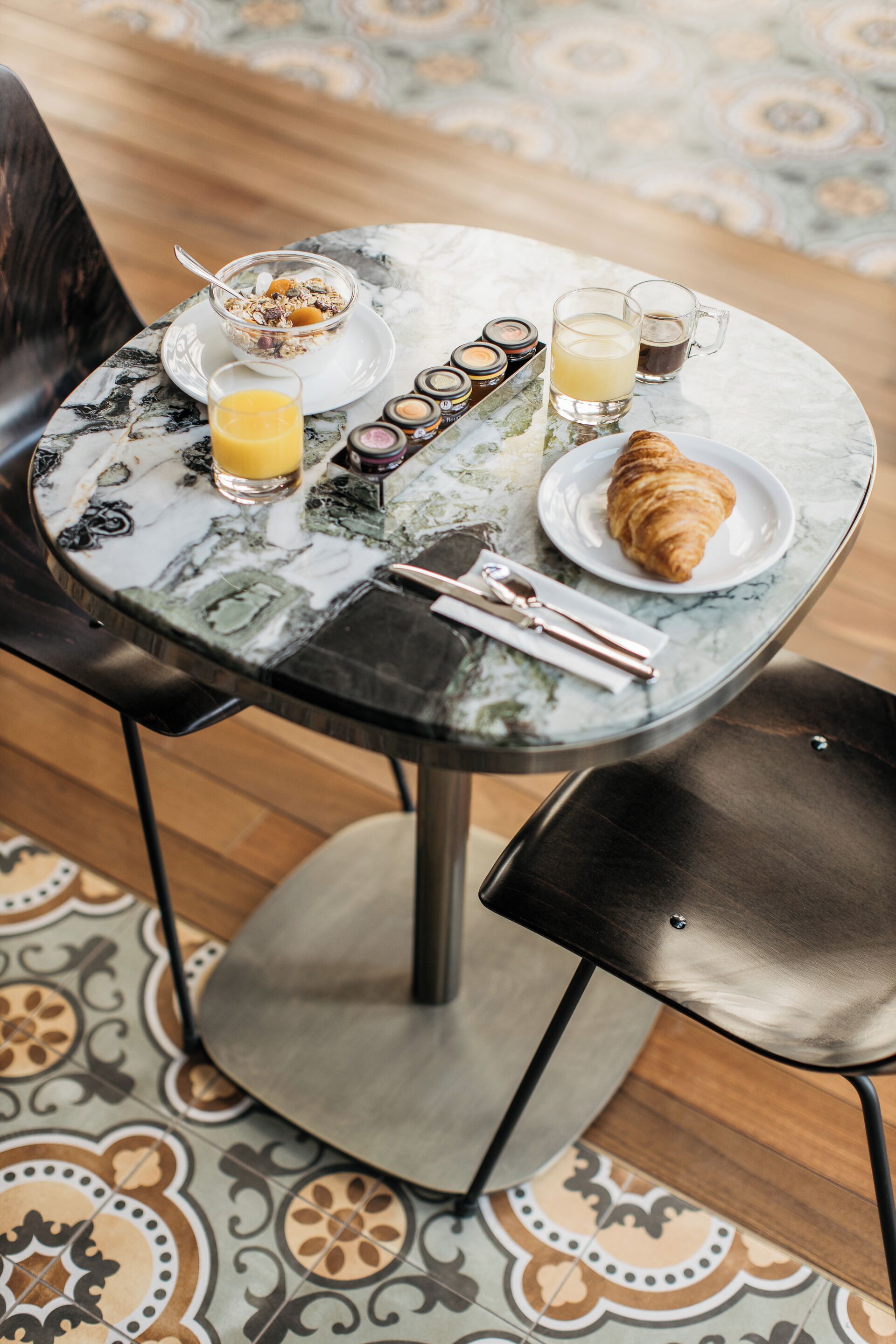A breakfast table with a croissant, a glass of orange juice, a bowl of cereal, and a set of condiments.