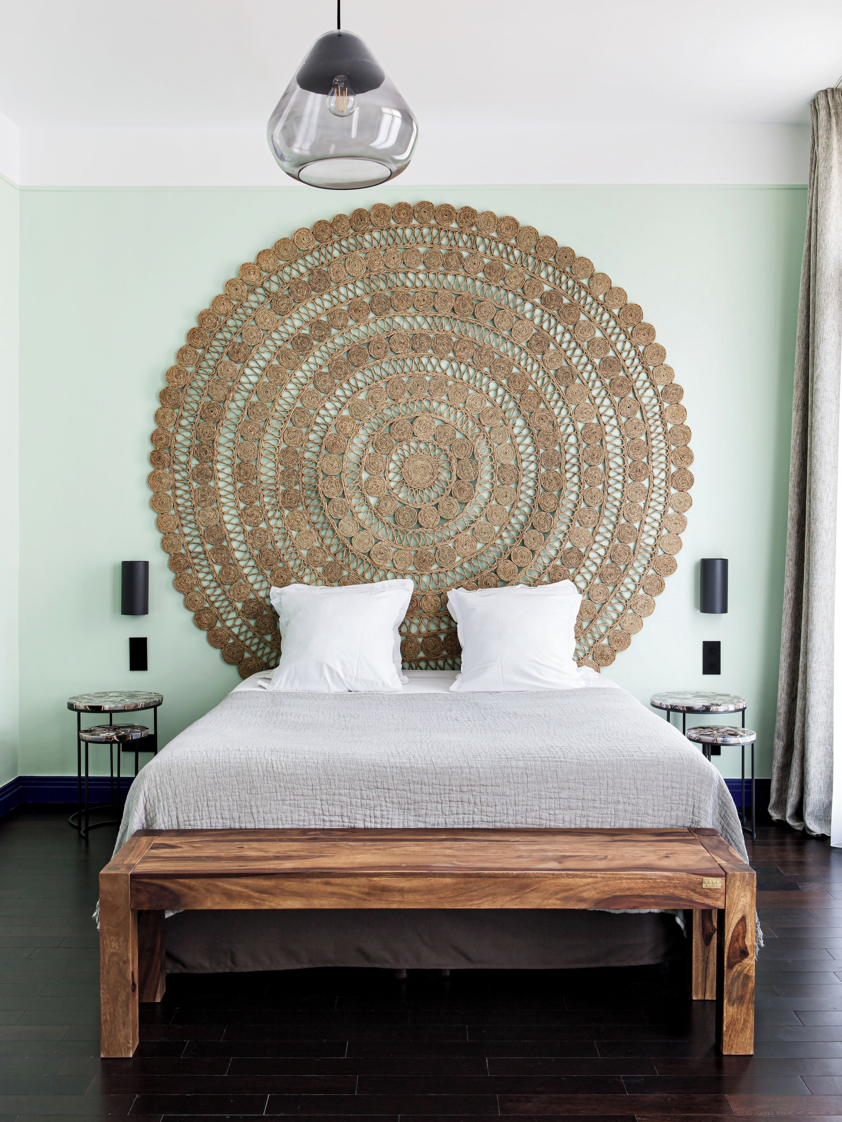 Un letto con struttura in legno, una grande testiera intrecciata, due comodini e un lampadario a sospensione.
