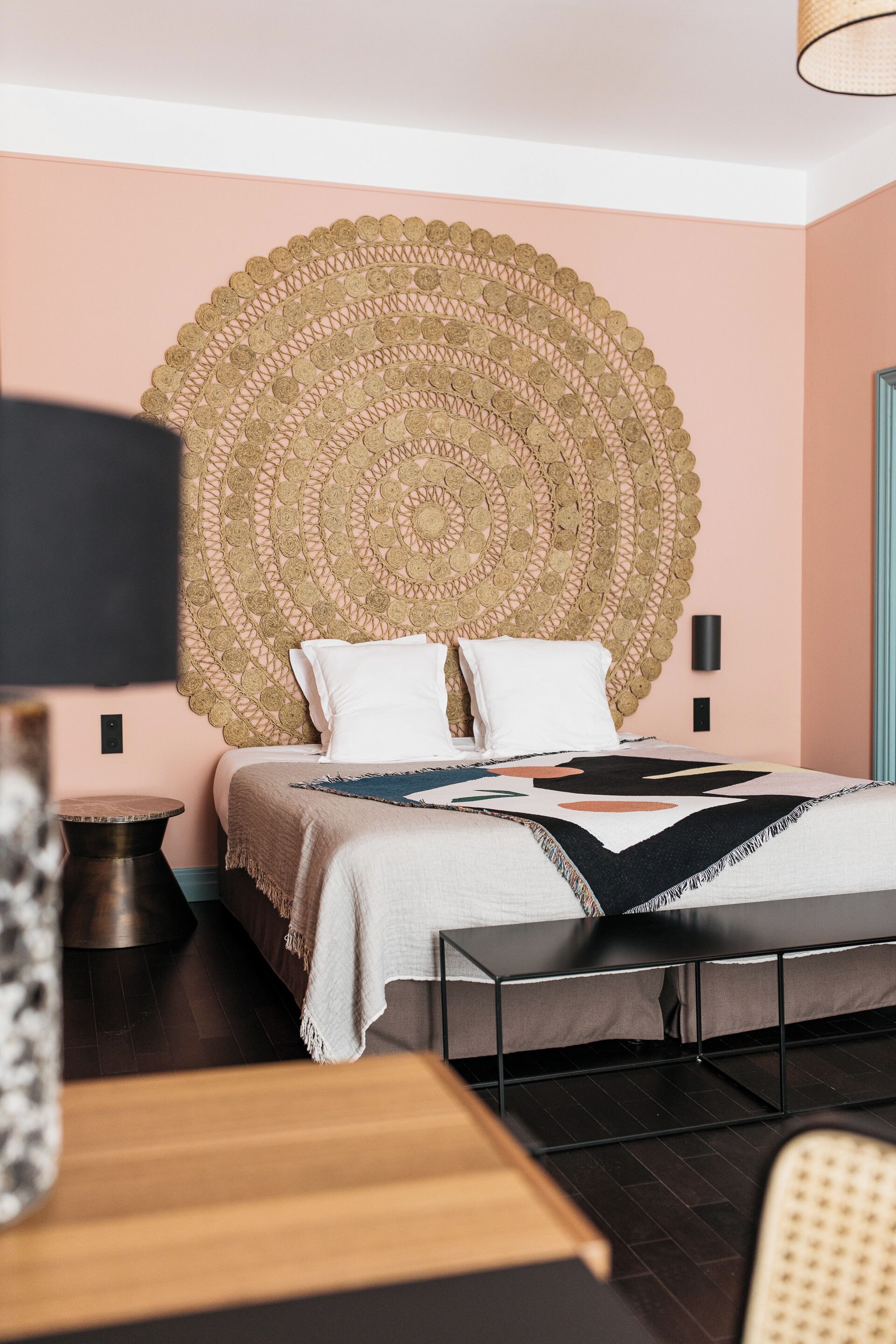 A bedroom with a large woven headboard, a bed with white bedding, a bedside table, and a lamp.