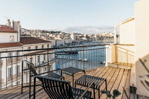 Un balcon doté d’un plancher en bois et de rampes en métal, offrant une vue sur une marina avec des bateaux et sur le paysage urbain.