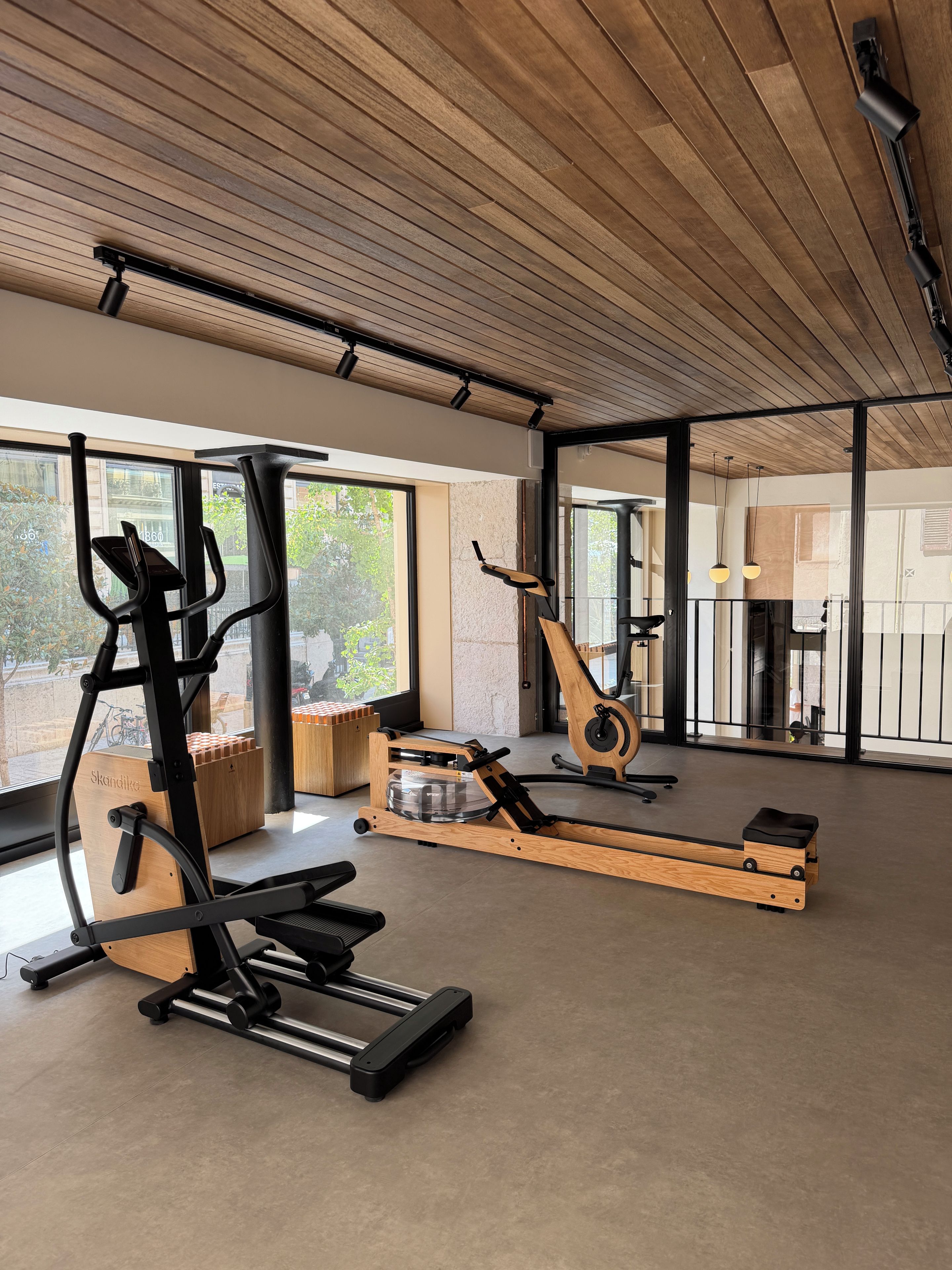 Un gimnasio con equipamiento de ejercicio, ventanas amplias y techo de madera.