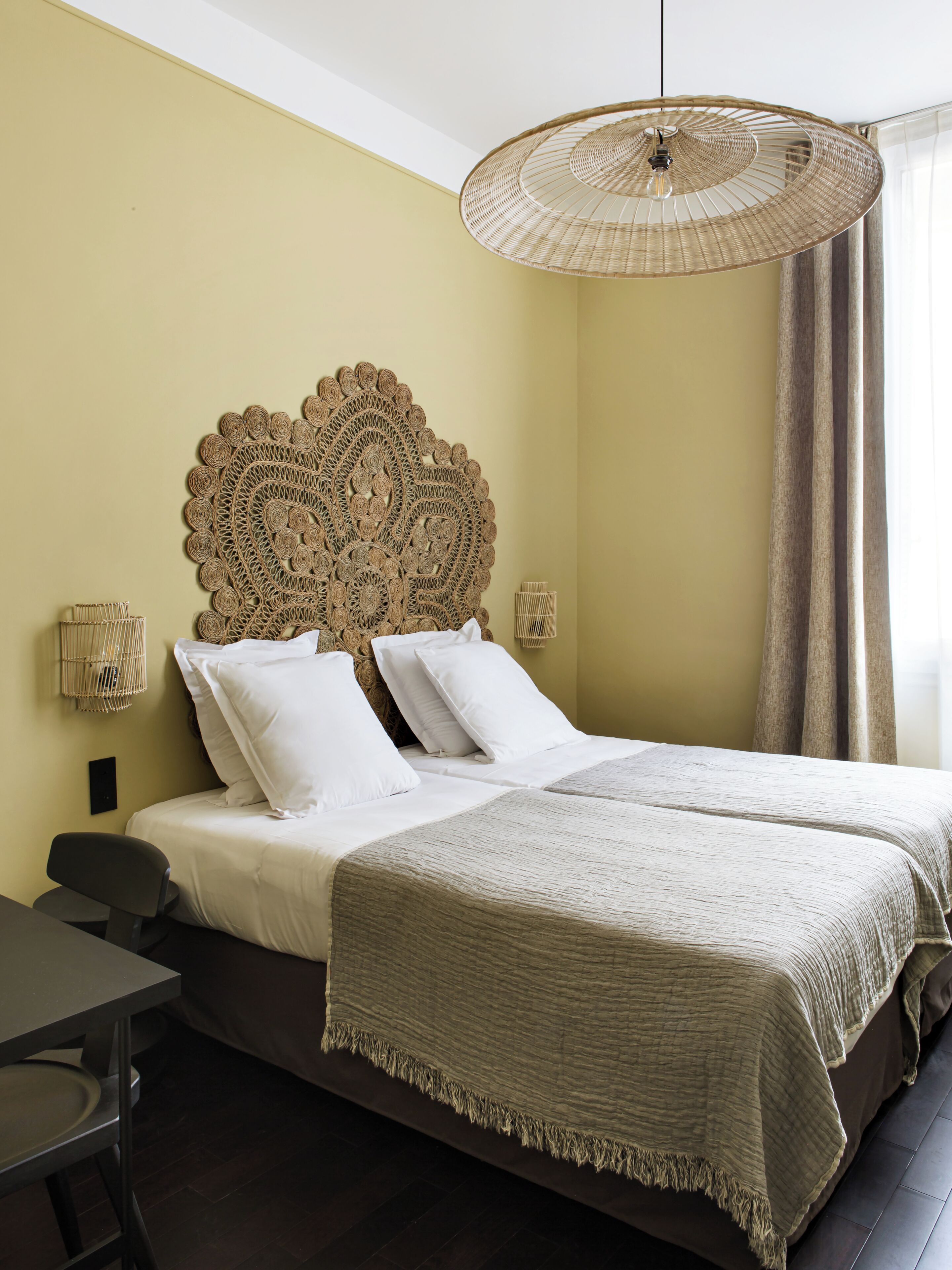 A double bed with a woven headboard, a bedside table, and a hanging light fixture.
