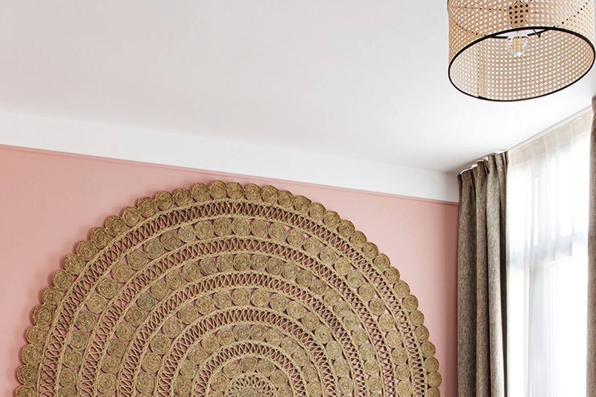 A bed with a circular woven headboard, a bedside table, and a hanging light fixture.