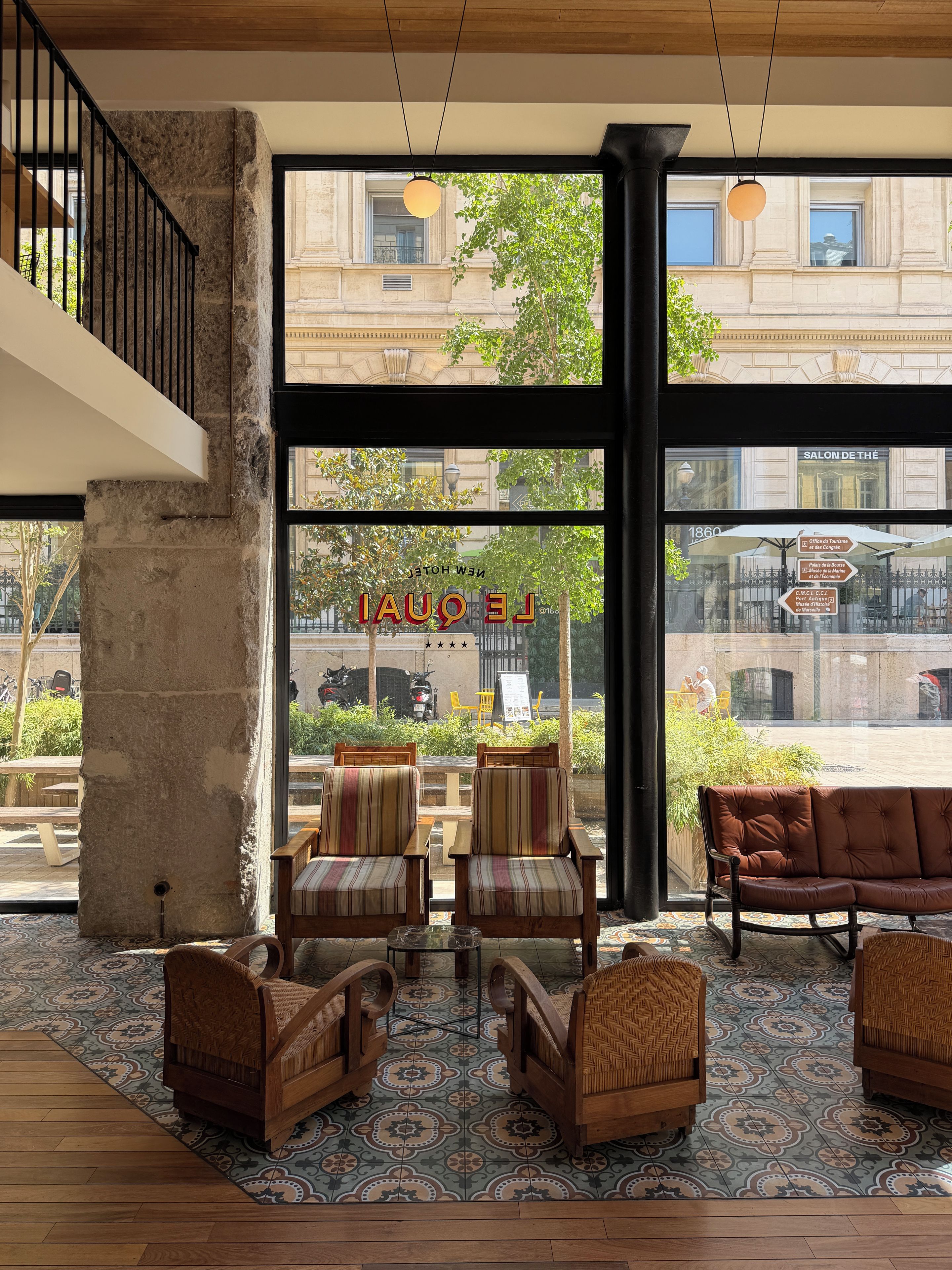 A hotel lobby with large windows, a stone pillar, and a seating area with striped and brown upholstered chairs.