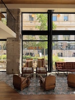 Un vestíbulo de hotel con amplios ventanales, un pilar de piedra y una zona de estar con sillones tapizados a rayas y en tonos marrones.