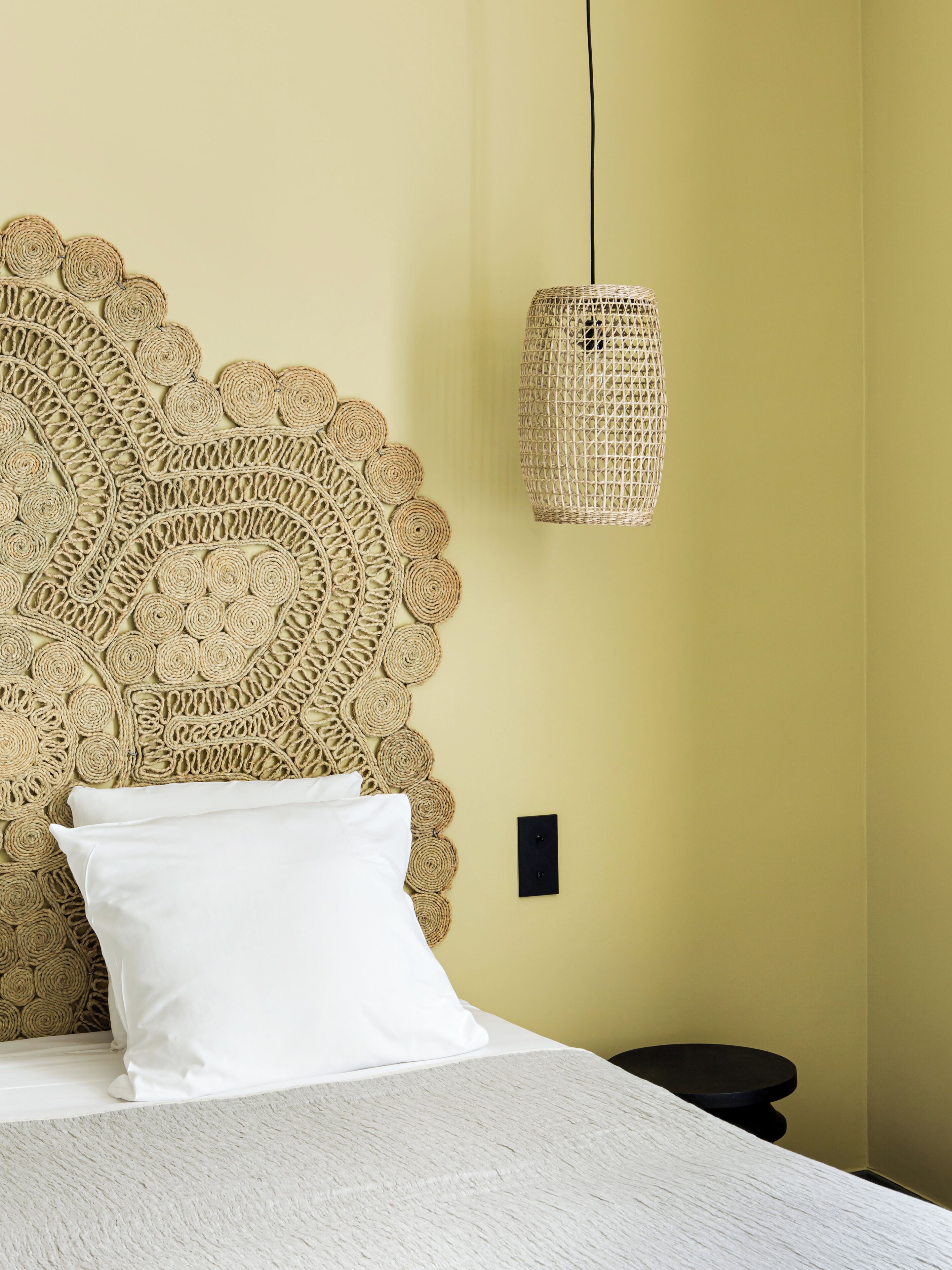 Una cama con cabecera de tejido, almohada blanca y colcha texturizada en blanco.