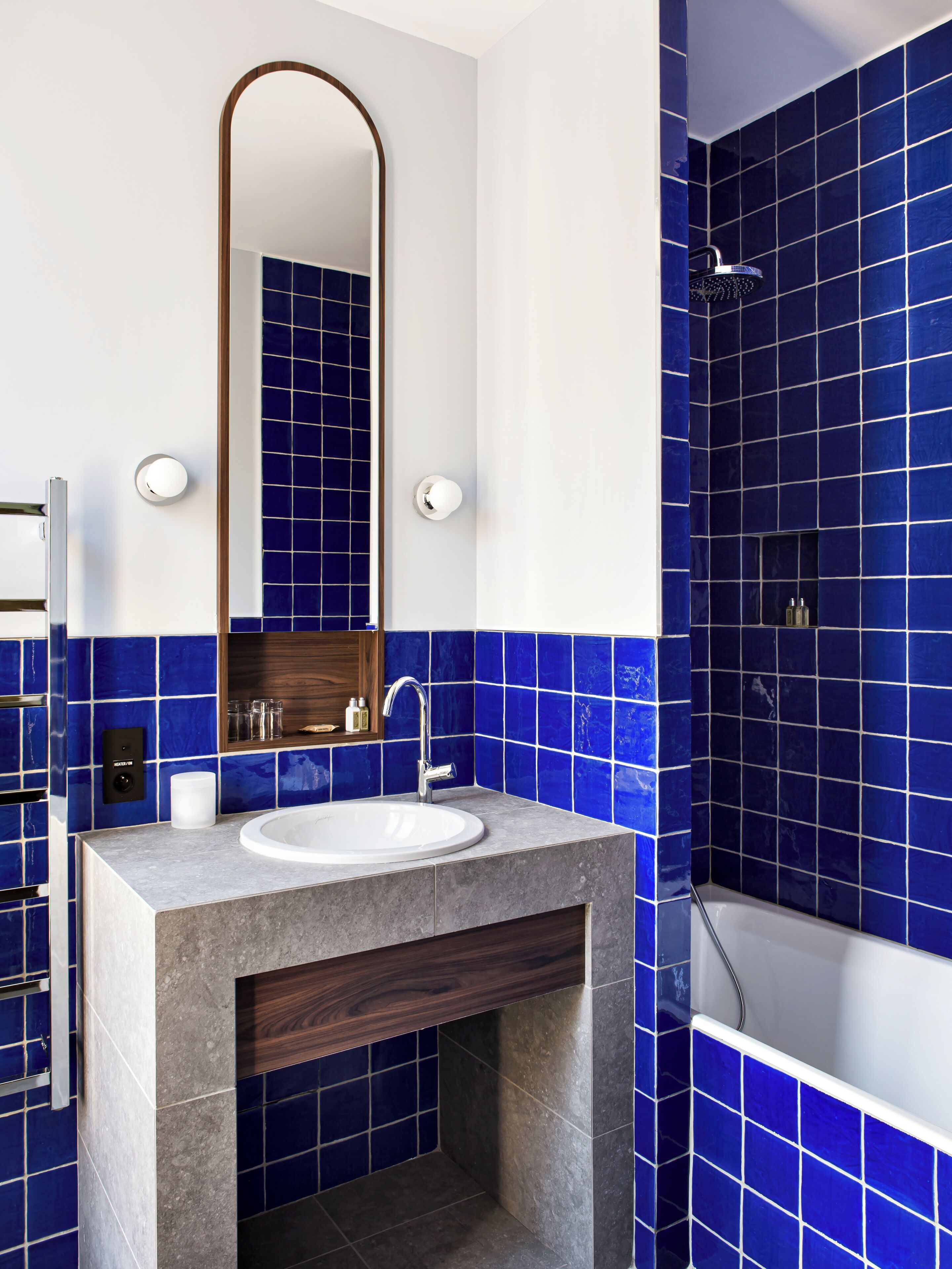 Un baño con un lavabo blanco, un tocador de madera, un espejo y una zona de ducha con azulejos azules.