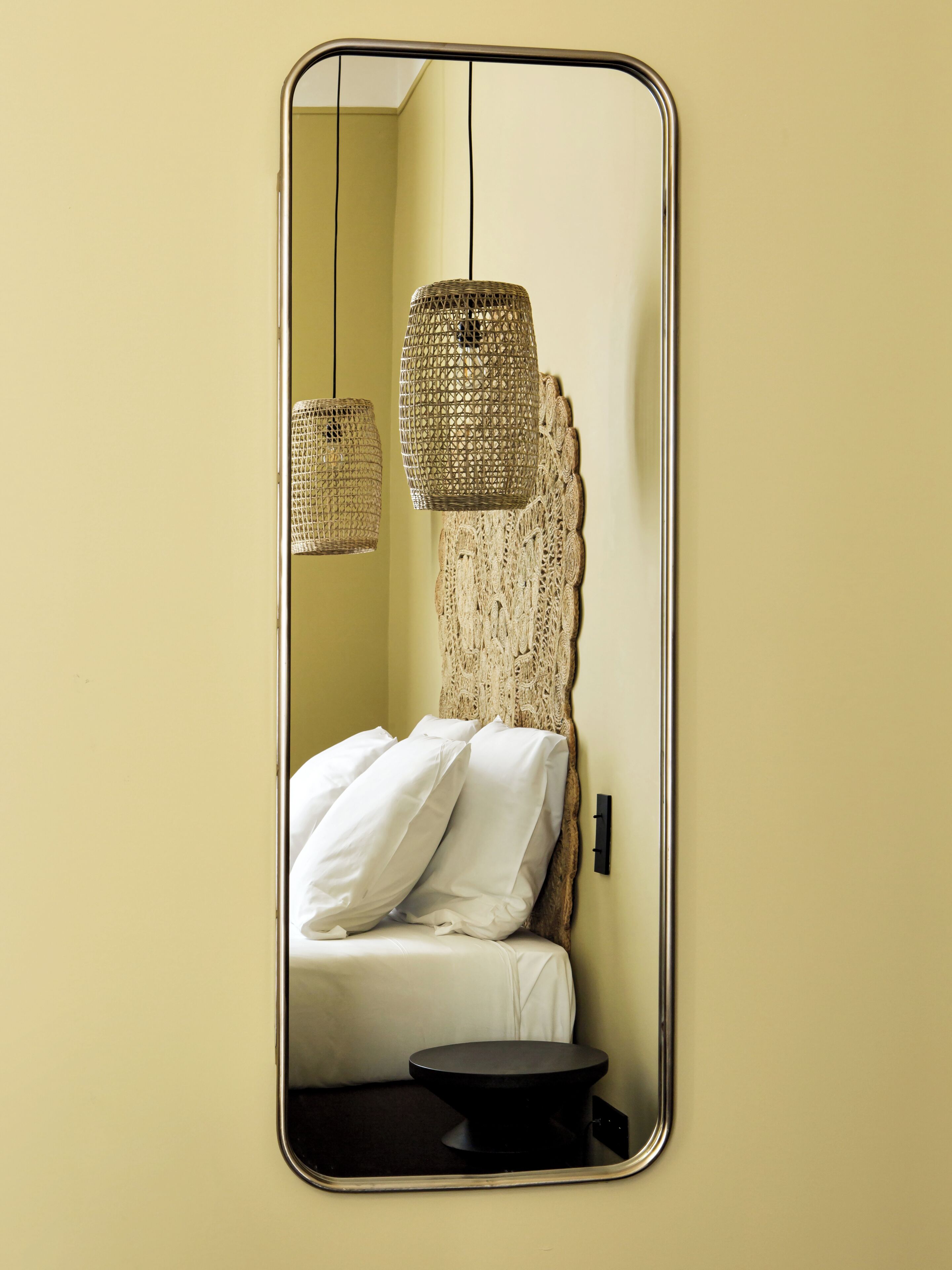 A room with a bed, a round black table, and two hanging wicker lamps.