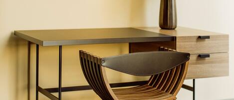 A modern desk with a wooden chair, a lamp, and wall art.