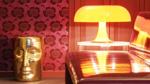 A room with a patterned wallpaper, a wooden door, a lamp, and a decorative object on the floor.
