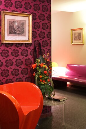 A room with a vibrant orange chair, a small table with a vase of flowers, and a pink couch. There are framed pictures on the wall. - Best Western Hotel Le Guilhem (Montpellier)