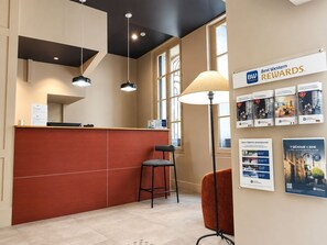 A reception area with a counter, a desk, a chair, and a lamp. There are posters on the wall advertising rewards. - Best Western Hotel Le Guilhem (Montpellier)
