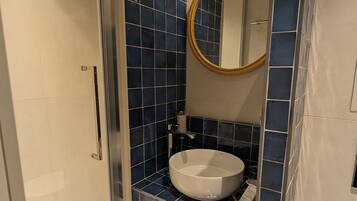 Une salle de bain avec une douche à parois de verre, un lavabo blanc et un miroir avec un cadre doré.