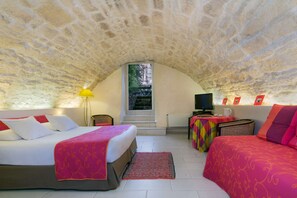 A cozy room with a stone ceiling, a bed with a red blanket, a sofa with a red cushion, a small table with a lamp, and a television. - Best Western Hotel Le Guilhem (Montpellier)