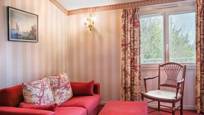 A room with a red sofa, a wooden chair, a small table, a painting on the wall, and a window with curtains. - Best Western Hotel Le Guilhem (Montpellier)