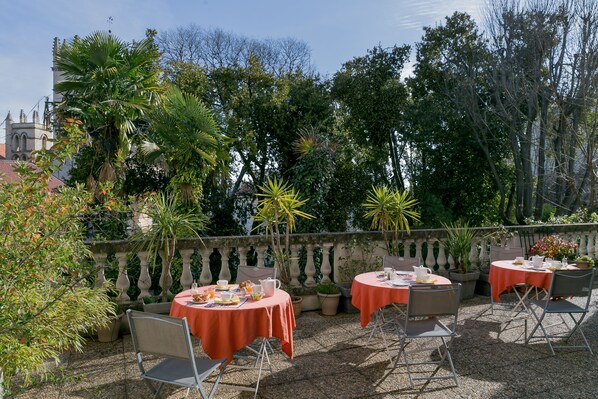 An outdoor patio with round tables covered with red tablecloths, surrounded by potted plants and chairs. - Best Western Hotel Le Guilhem (Montpellier)