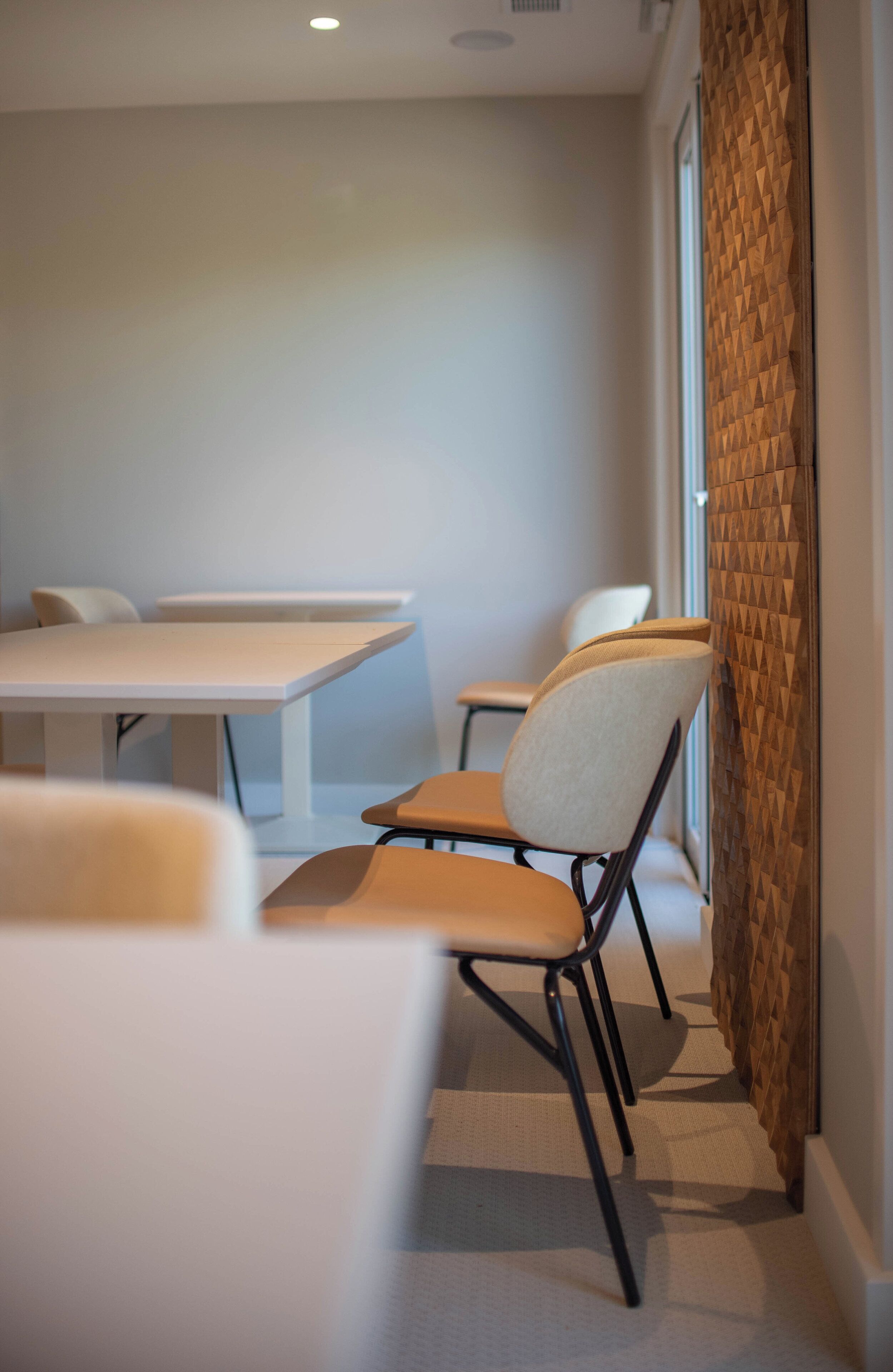 A conference room with white tables and chairs, a patterned wall, and a window with blinds.