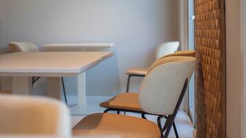 A conference room with white tables and chairs, a patterned wall, and a window with blinds.