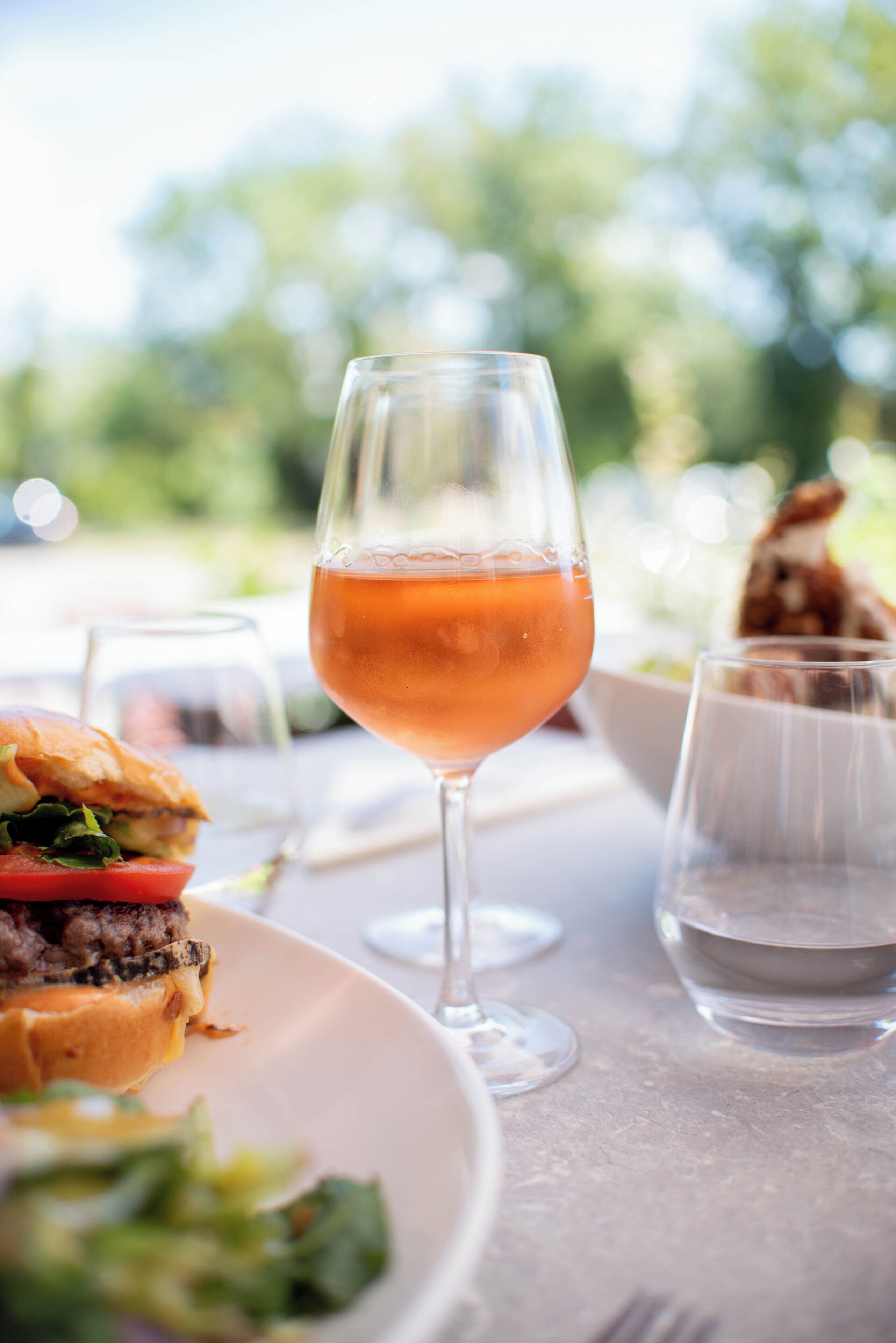 A dining table with a glass of rosé wine, a sandwich, and a glass of water.