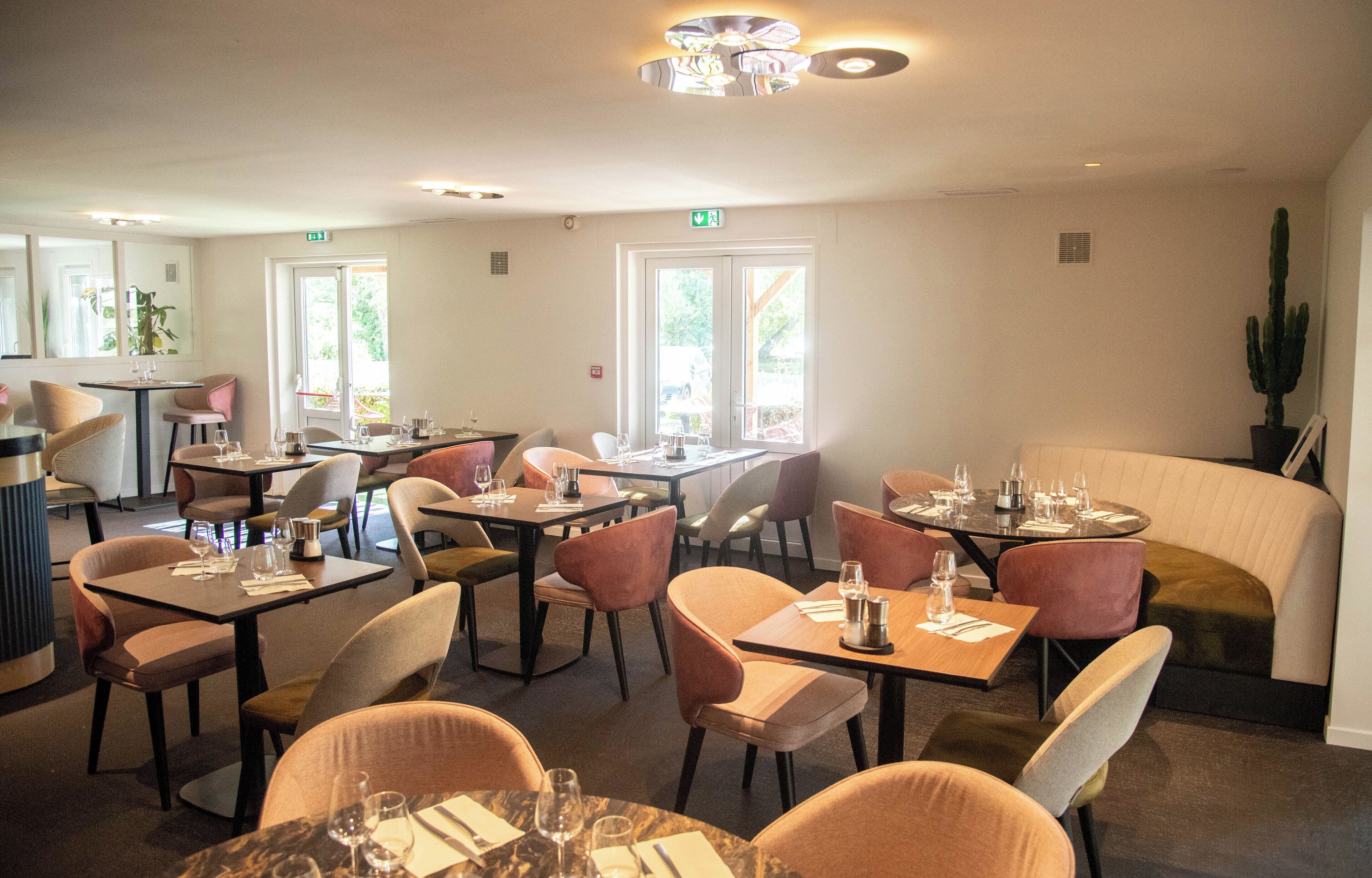 En restaurang med flera bord och stolar, en bardisk och ett stort fönster med utsikt över grönområden.