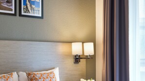 Habitación de hotel con cama, almohadas, mesita de noche con lámpara y pared decorada con cuadros.