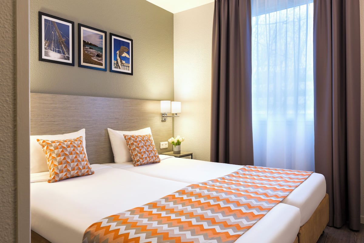 A hotel room with a large bed, two pillows, a nightstand with a lamp, and framed pictures on the wall.