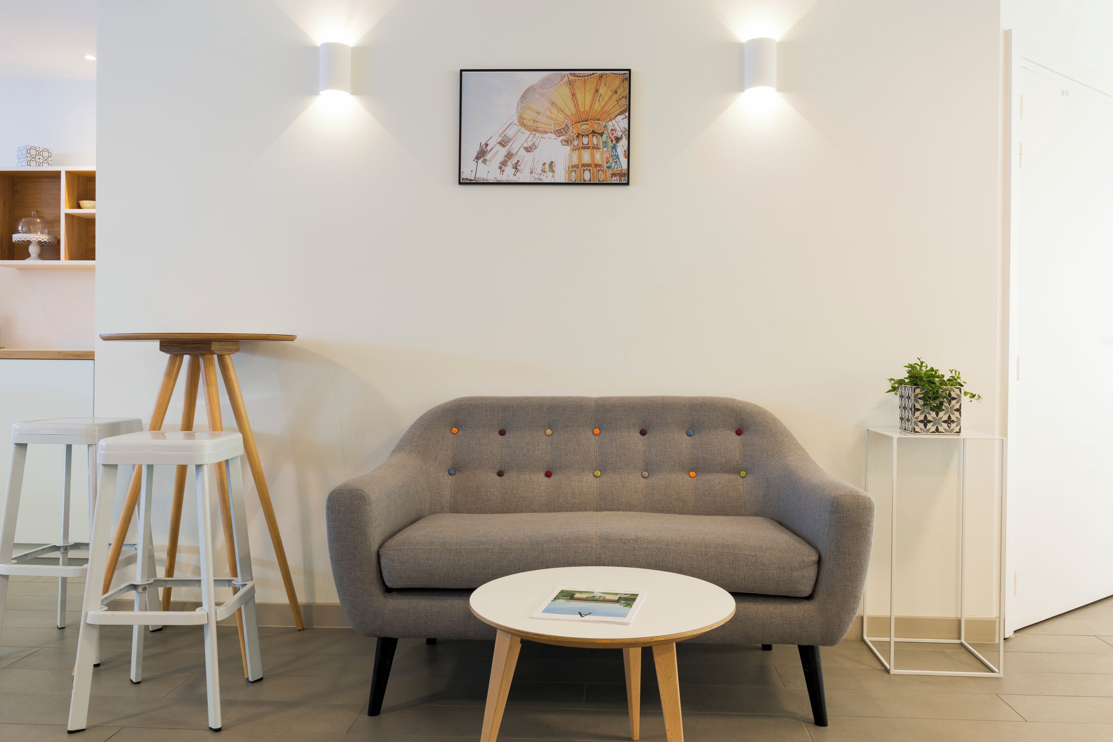 Une pièce avec un canapé gris, une petite table ronde, une chaise blanche et un tableau accroché au mur.