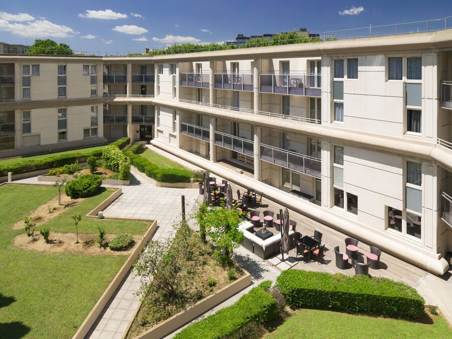 A multi-story hotel with outdoor seating areas, a landscaped garden, and a modern architectural design.