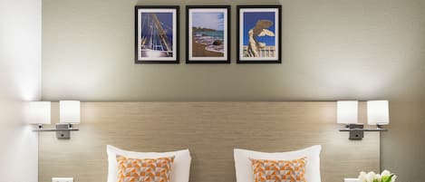 A hotel room with a wooden headboard, two pillows with geometric patterns, a bed with a chevron-patterned bedspread, a nightstand with a vase of flowers, and three framed pictures on the wall.
