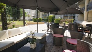 Un espacio al aire libre con mobiliario de mimbre, un sofá blanco y sombrillas que dan sombra.