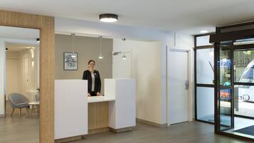 A reception area with a receptionist, a wooden-framed mirror, a white reception desk, and a glass door leading outside.